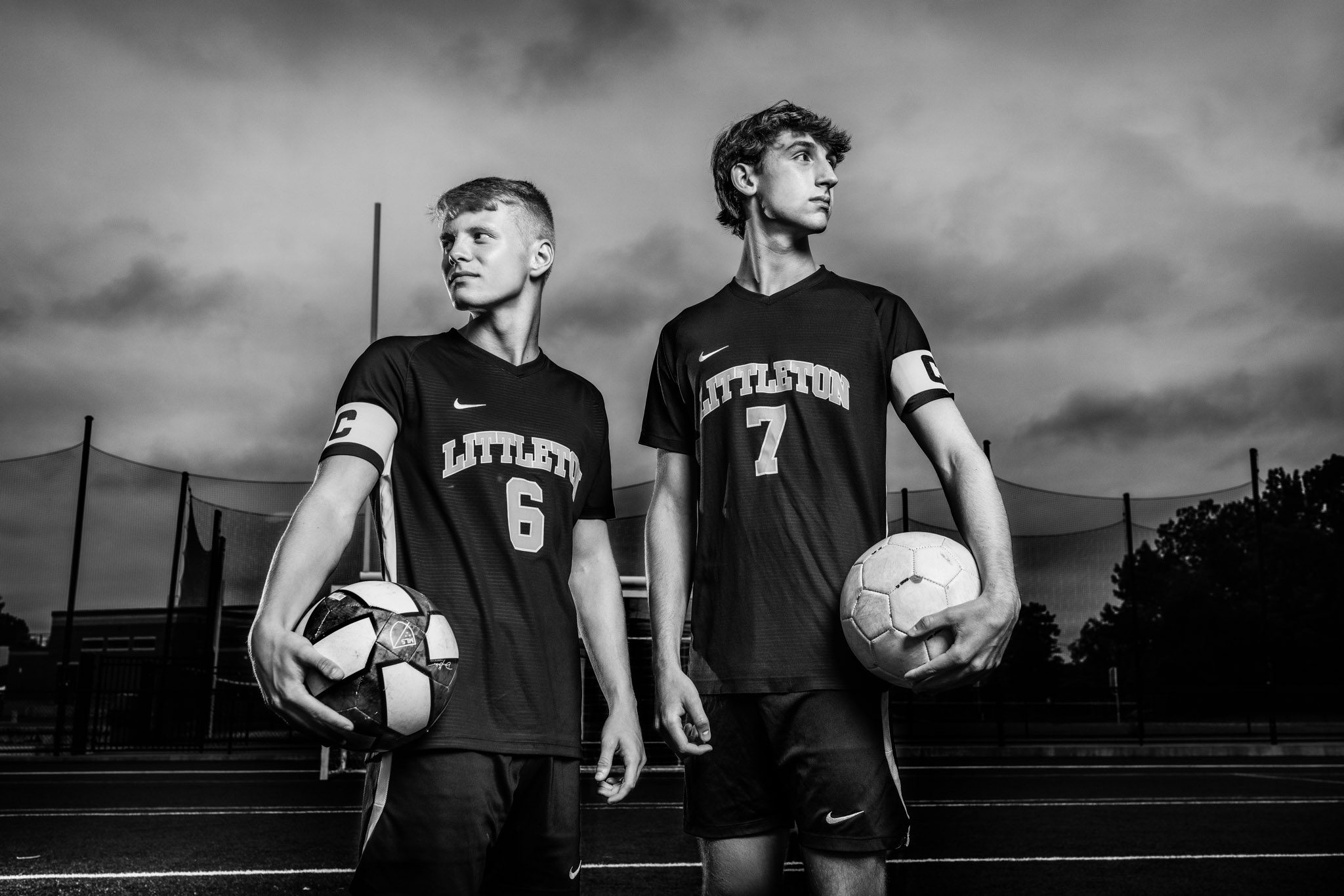 Black and white senior portrait of two young men in soccer uniforms holding soccer balls on a field in Littleton Massachusetts
