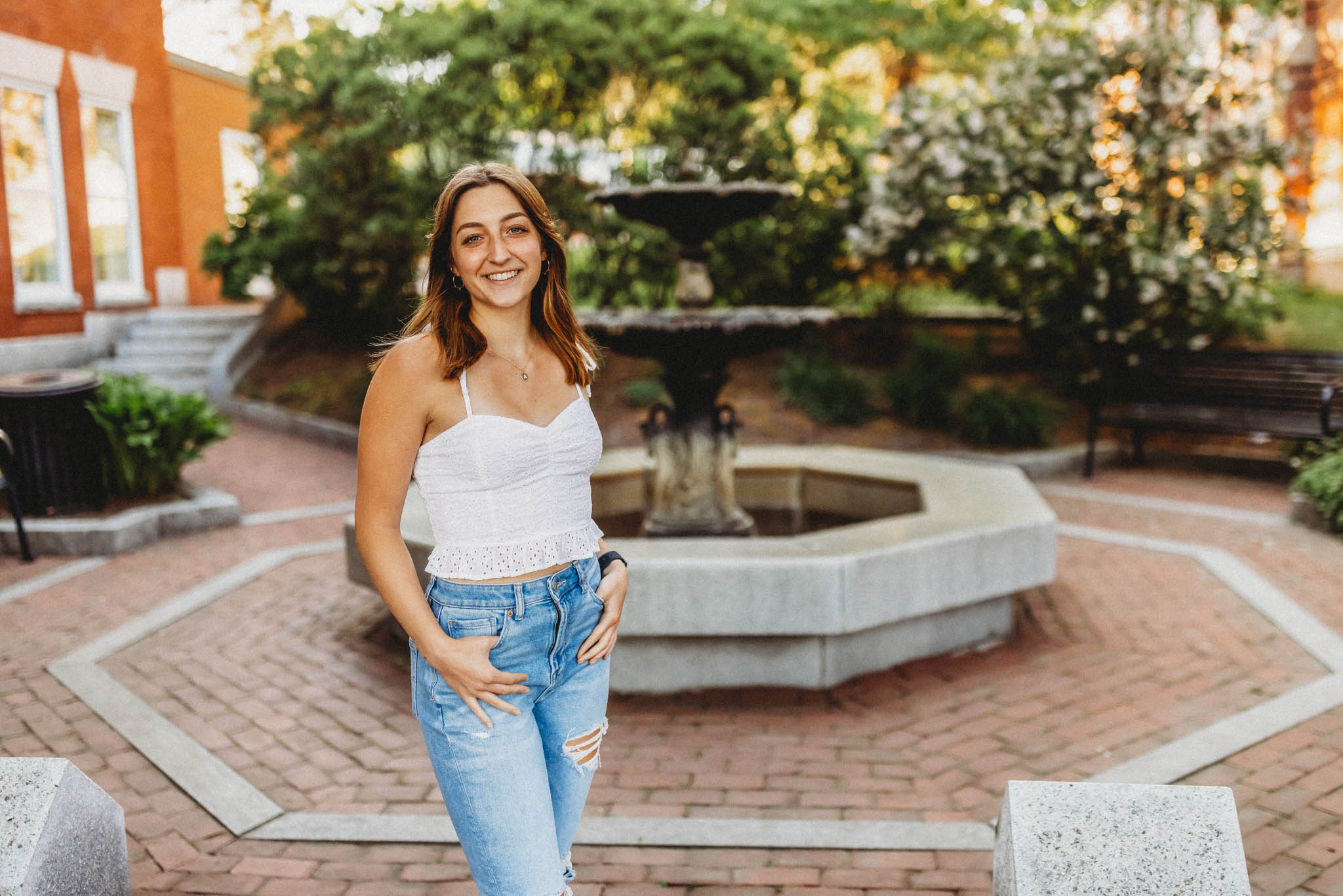Summer senior portrait of a young woman in a lace top and jeans standing in front of a fountain in Massachusetts