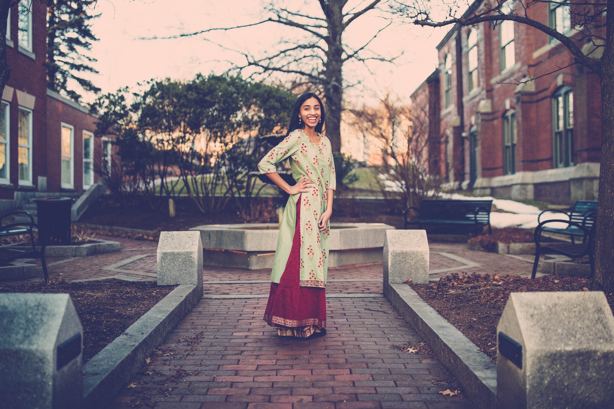 High school senior portrait of a young Indian girl wearing traditional clothing in a courtyard with a fountain and brick sidewalks in Massachusetts photographed by Sean Wytrwal of J&S Photography