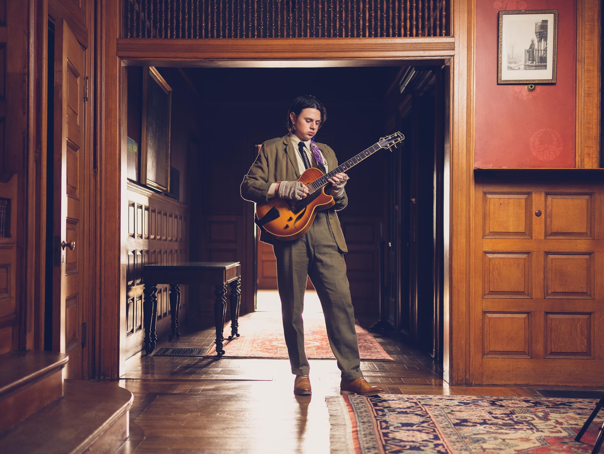 Senior portrait of a young man wearing a suit and playing a guitar inside a historic mansion in Massachusetts