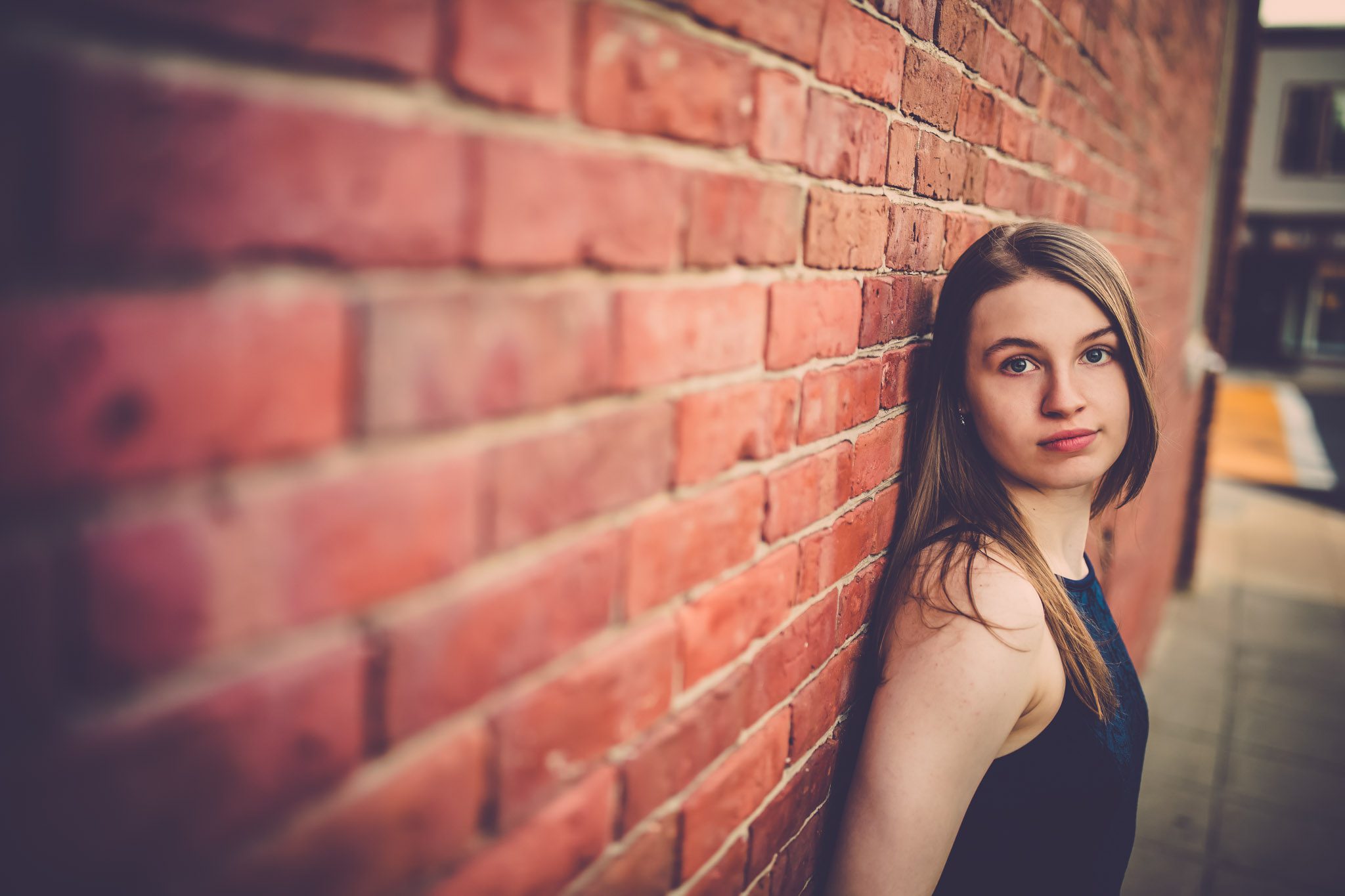 Senior portrait of a young woman in a blue dress leaning against a brick wall in a city in Ayer Massachusetts
